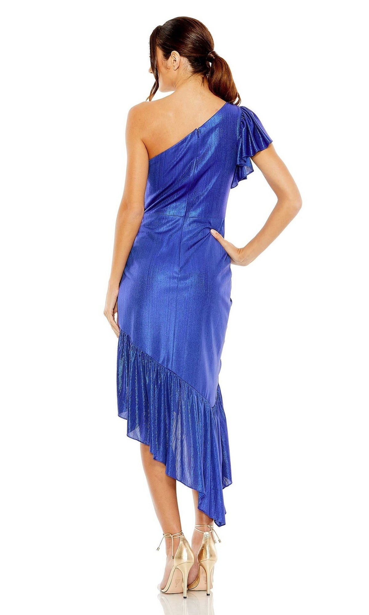 A woman stands with her back to the camera, wearing the Short Wedding Guest Dress 27075 by Mac Duggal—a shiny blue metallic one-shoulder dress with a ruffled asymmetric hem—and beige high-heeled shoes.